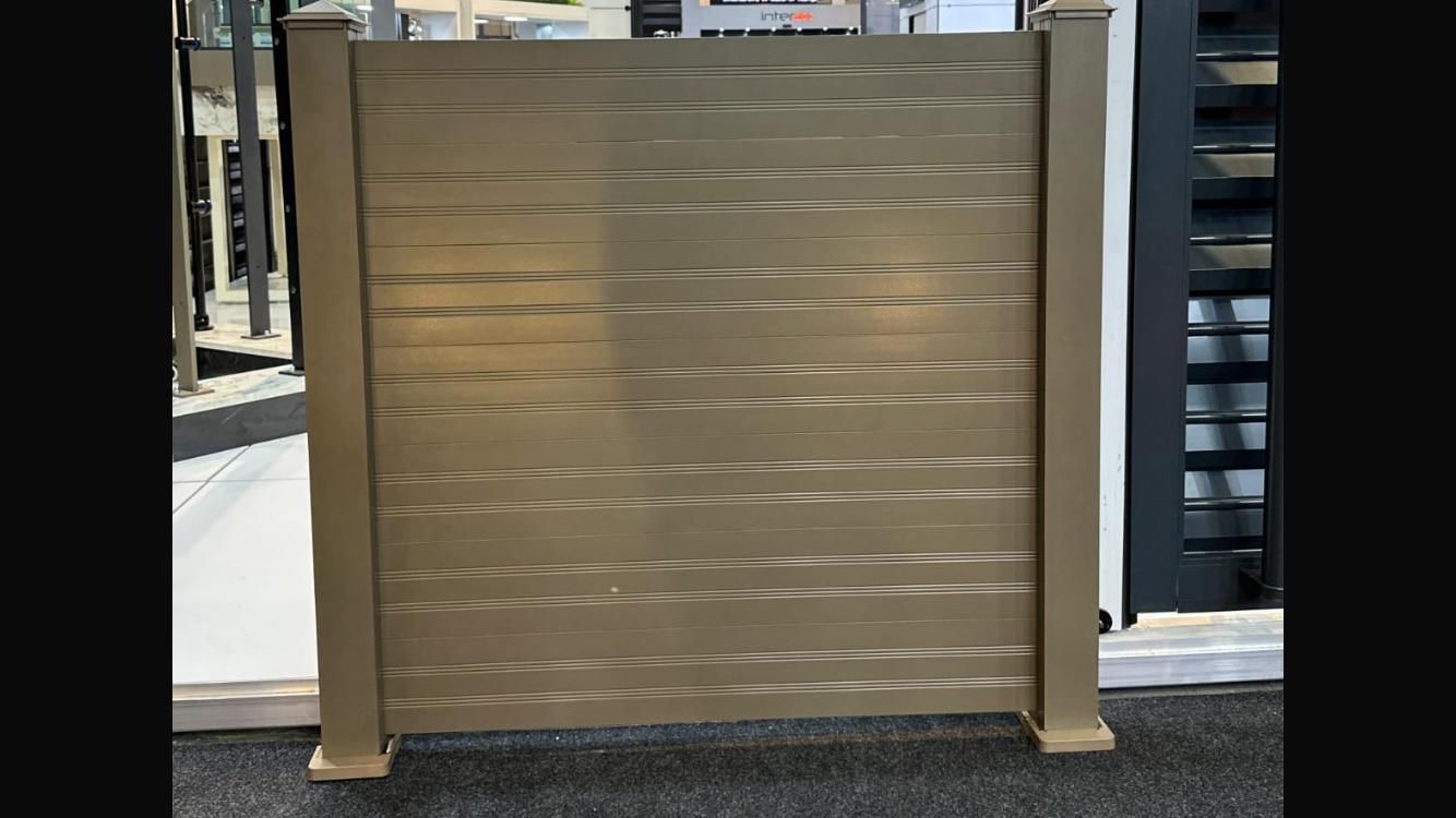 Dark gray louvered fence on concrete base with lawn and trees