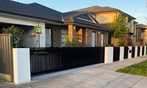 Black vertical slat aluminum fence with white pillars in front of modern brick house, sidewalk and suburban street